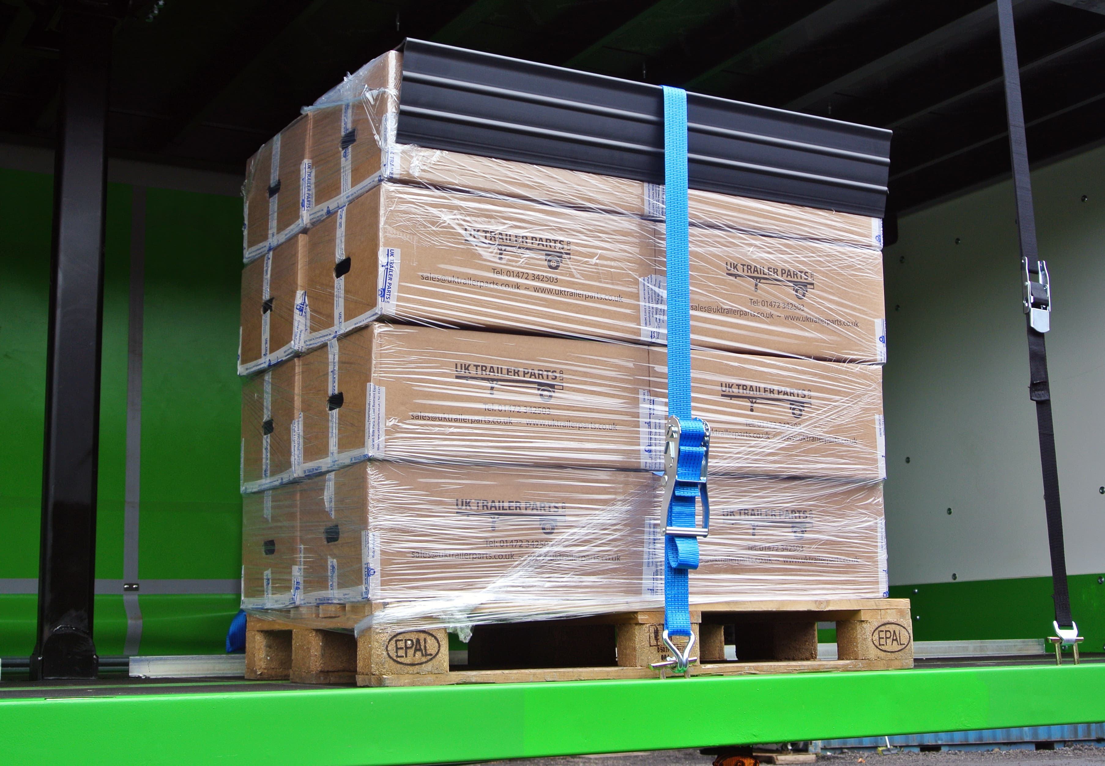 Extruded heavy duty plastic corner protector on top of a pallet of boxes. Held in place by a 5000kg ratchet strap.